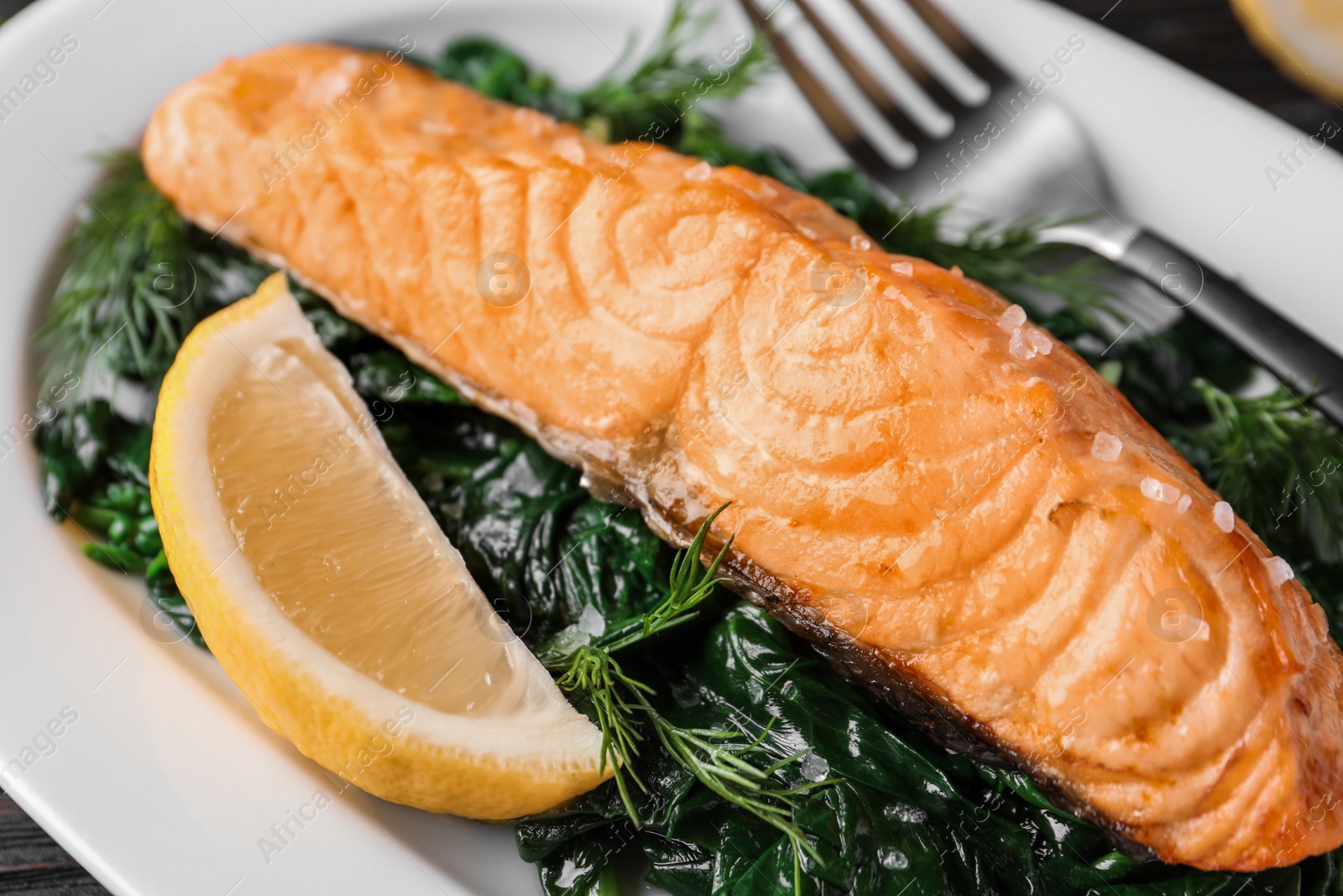 Photo of Tasty salmon with spinach and lemon on plate, closeup