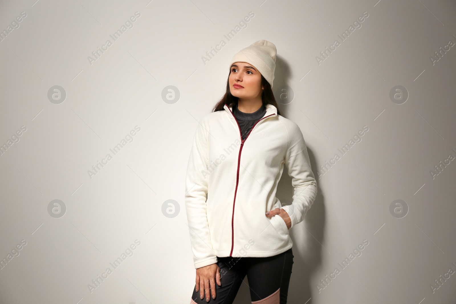 Photo of Woman wearing fleece jacket and hat on light grey background. Winter sport clothes