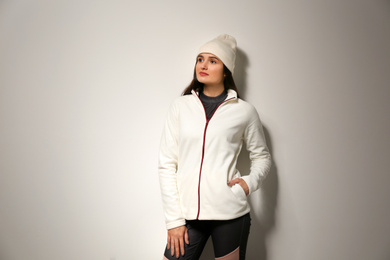 Photo of Woman wearing fleece jacket and hat on light grey background. Winter sport clothes