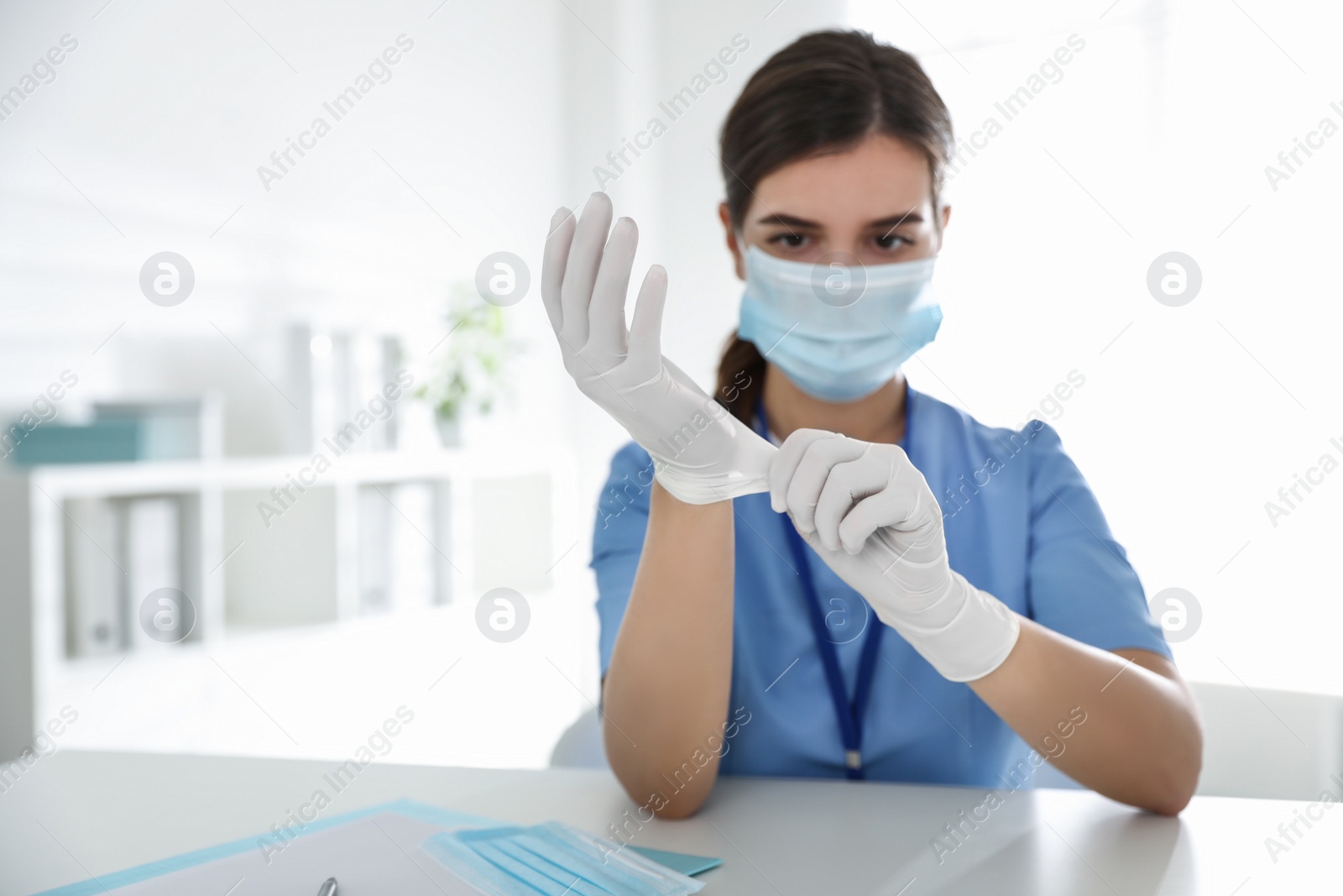 Photo of Doctor in protective mask putting on medical gloves at table in office