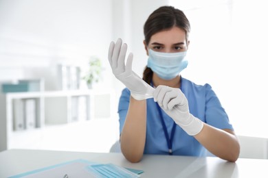 Doctor in protective mask putting on medical gloves at table in office