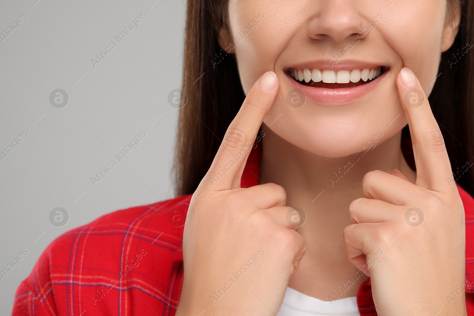 Photo of Woman showing her clean teeth and smiling on light grey background, closeup