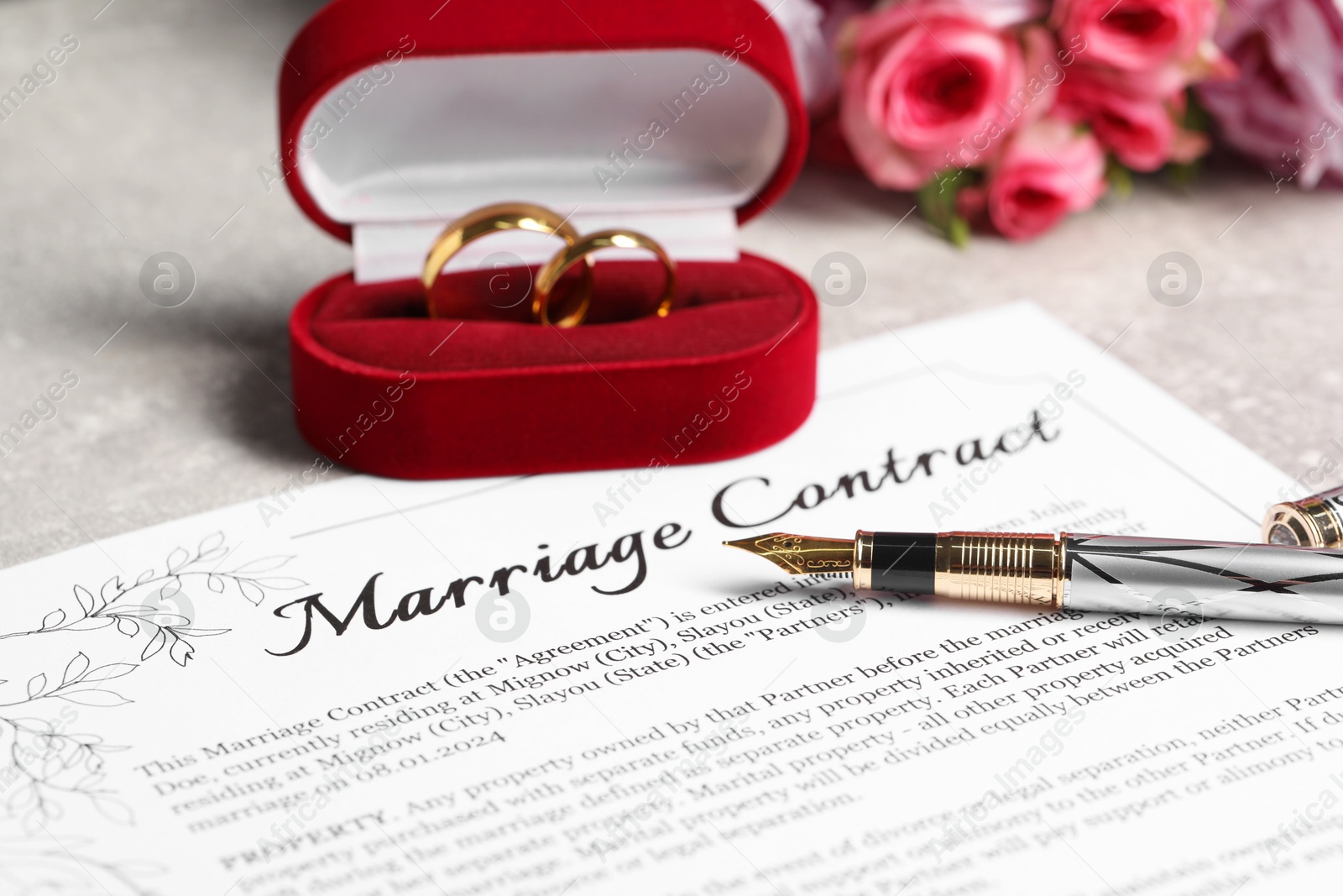 Photo of Marriage contract, fountain pen, golden wedding rings and flowers on grey table, closeup