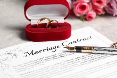 Marriage contract, fountain pen, golden wedding rings and flowers on grey table, closeup