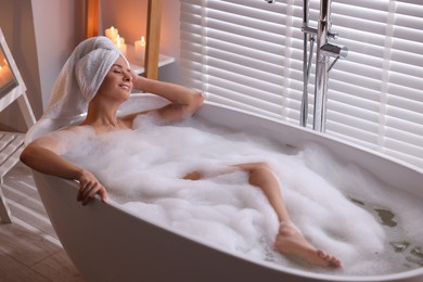 Photo of Beautiful woman taking bath in tub with foam indoors. Romantic atmosphere