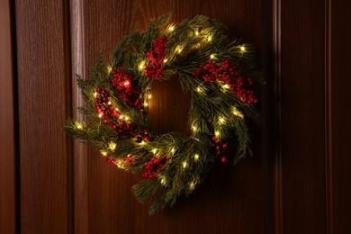 Photo of Beautiful Christmas wreath with red berries and fairy lights hanging on wooden door