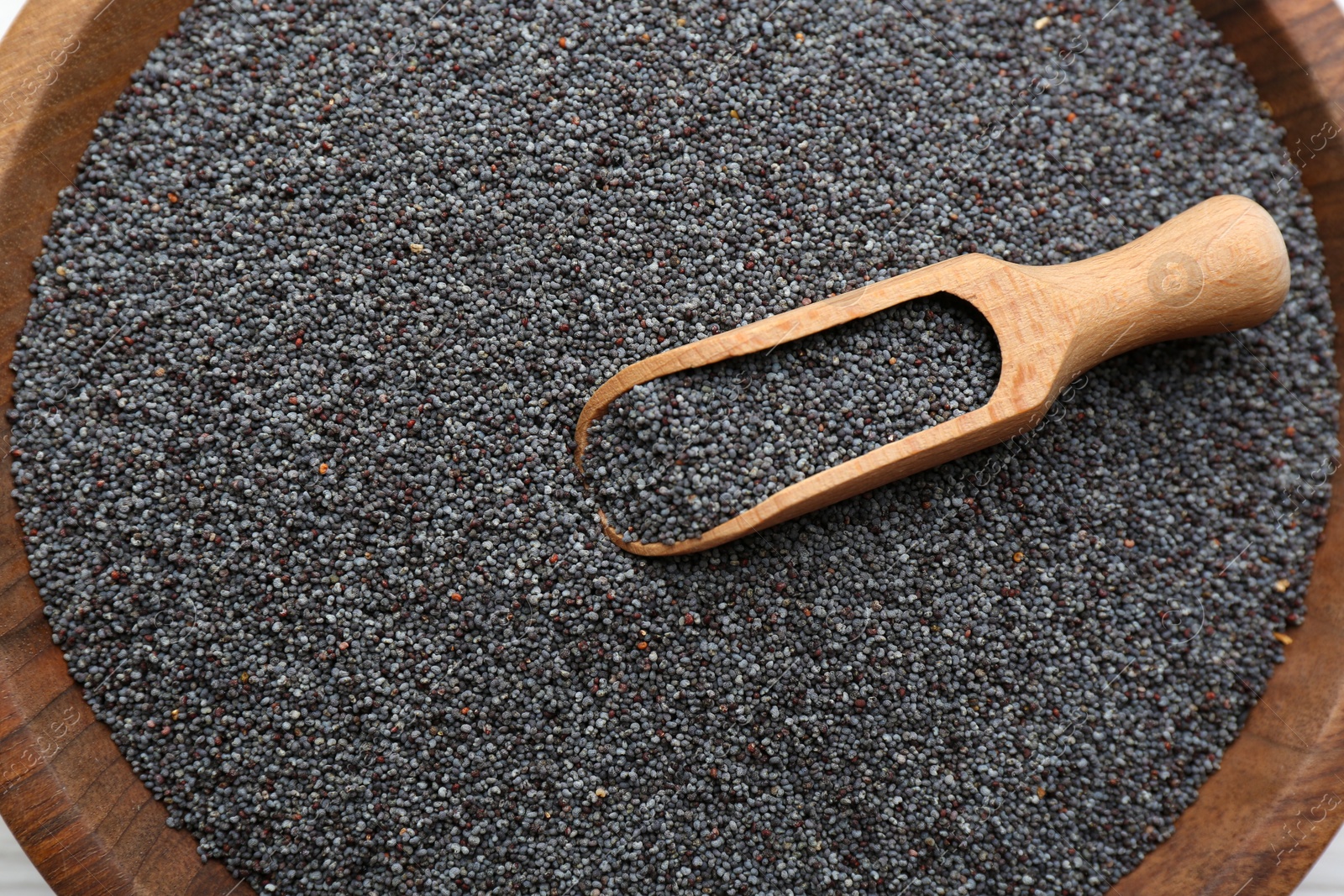 Photo of Poppy seeds and wooden scoop in bowl, closeup