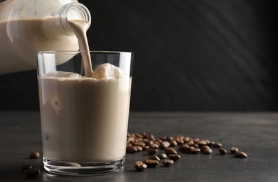 Photo of Pouring coffee cream liqueur into glass at grey table, closeup. Space for text