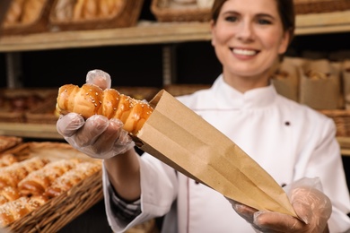 Photo of Baker putting fresh bun into paper bag in store