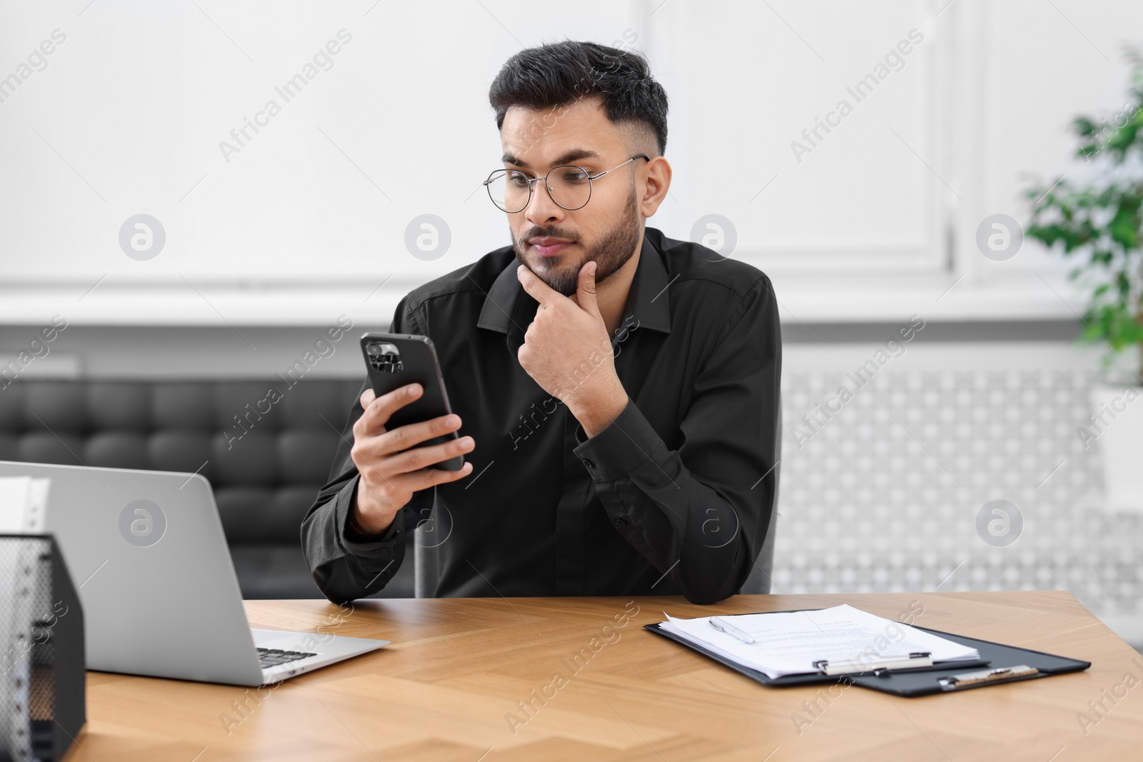 Photo of Handsome young man using smartphone at wooden table in office