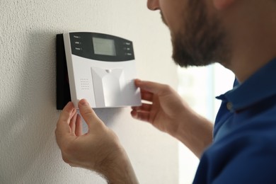 Photo of Man installing home security system on white wall in room, closeup