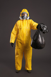 Photo of Woman in chemical protective suit holding trash bag on grey background. Virus research
