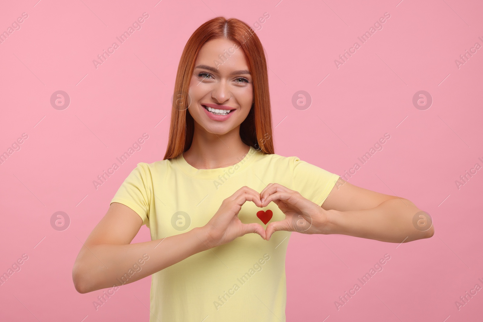 Photo of Beautiful happy woman making heart with her hands on pink background