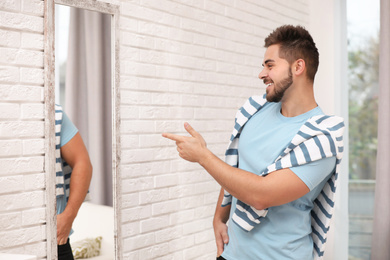 Photo of Young man looking at himself in large mirror at home