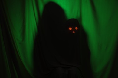 Photo of Silhouette of creepy ghost with skull behind dark green cloth