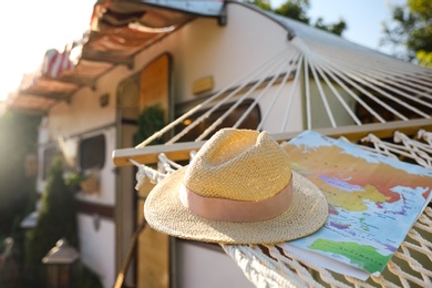 Comfortable hammock with hat and world map near motorhome outdoors on sunny day