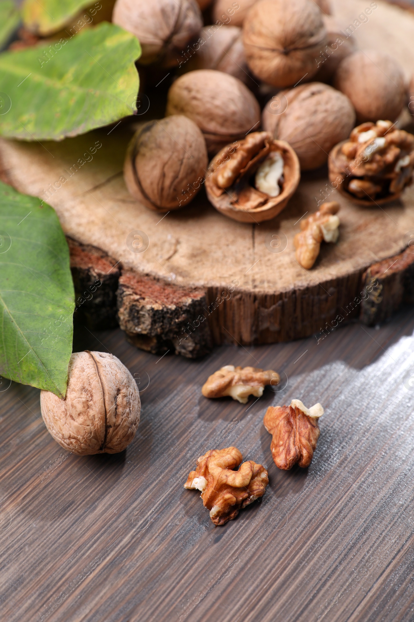 Photo of Tasty walnuts and fresh leaves on wooden table, closeup
