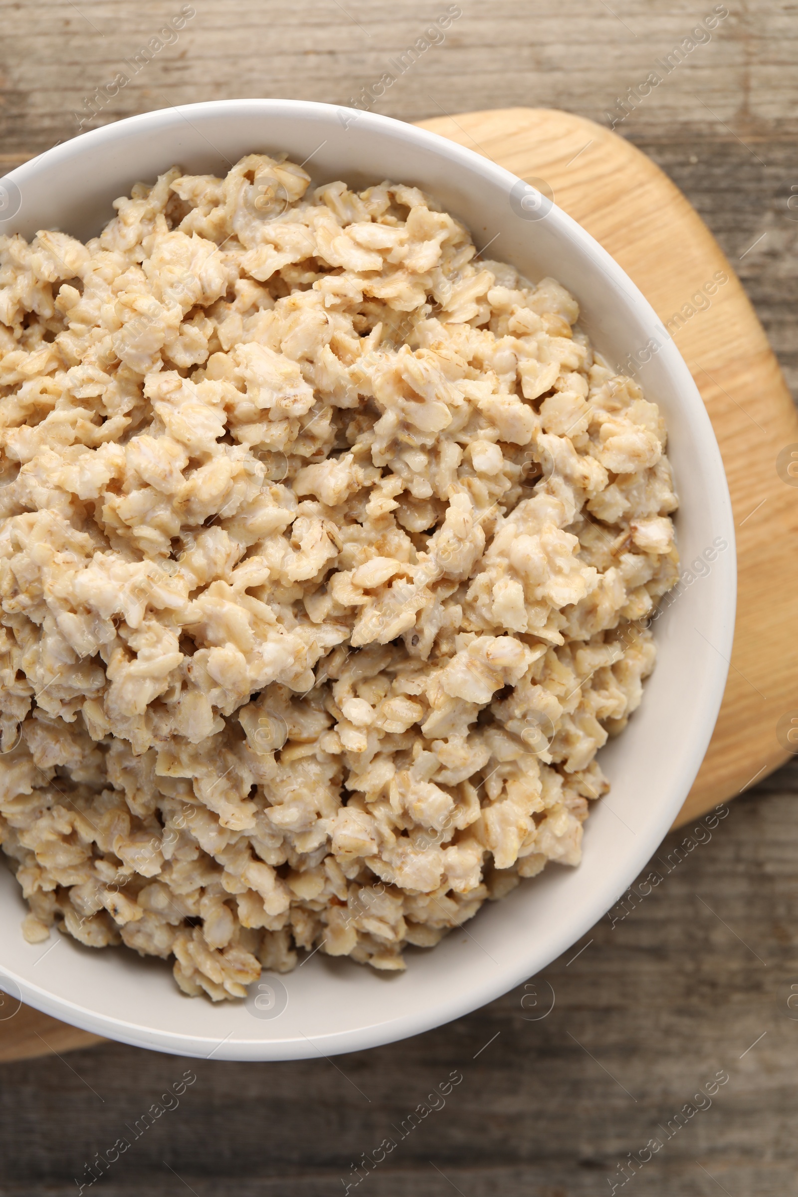 Photo of Tasty boiled oatmeal in bowl on wooden table, top view