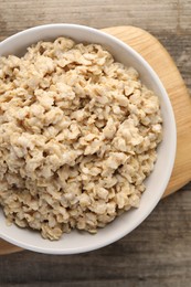 Photo of Tasty boiled oatmeal in bowl on wooden table, top view