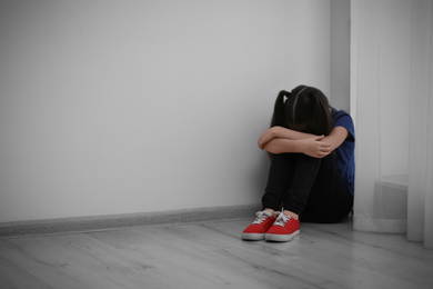 Photo of Sad little girl sitting on floor indoors, space for text. Child in danger