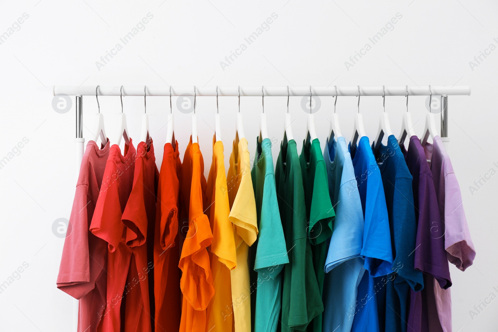 Photo of Rack with bright clothes on white background. Rainbow colors