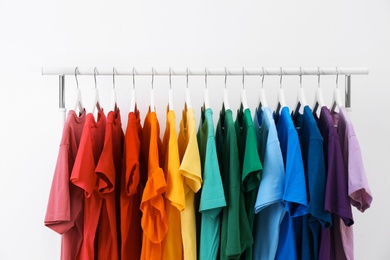 Rack with bright clothes on white background. Rainbow colors