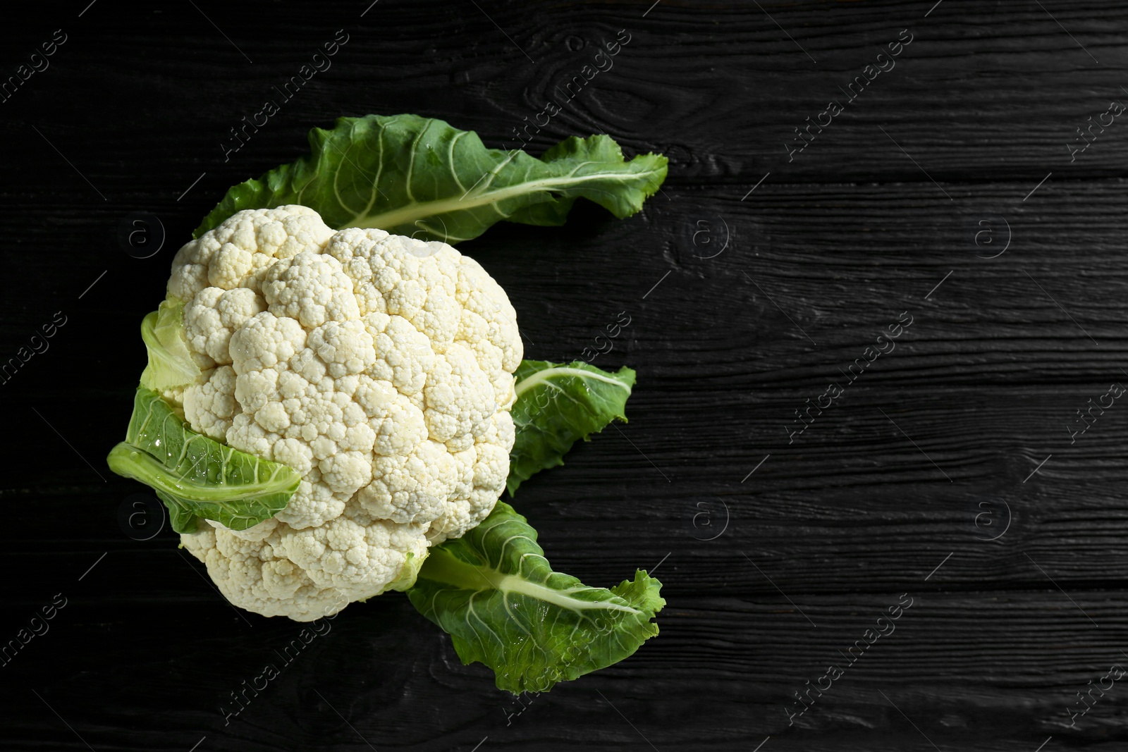 Photo of Fresh whole cauliflower on black wooden table, top view. Space for text