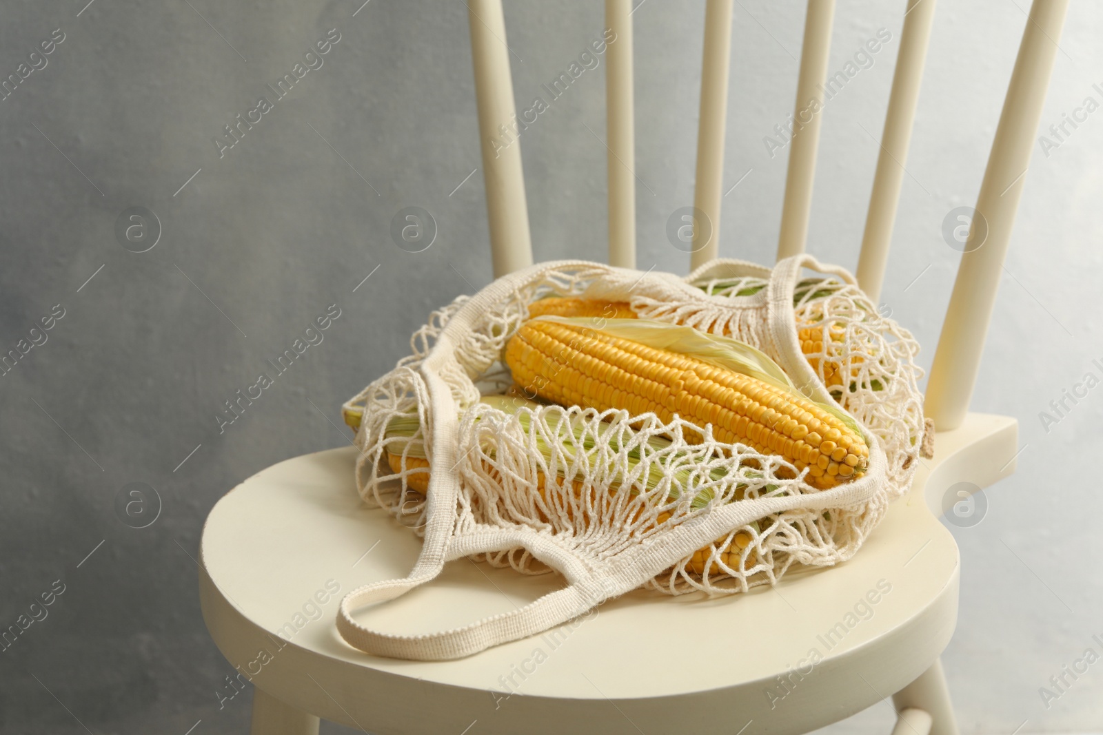 Photo of Bag of corn cobs on chair against grey background