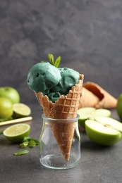 Composition with delicious spirulina ice cream cone on table against grey background