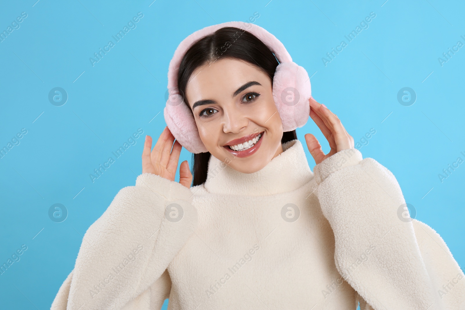 Photo of Beautiful young woman wearing earmuffs on light blue background