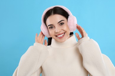 Beautiful young woman wearing earmuffs on light blue background