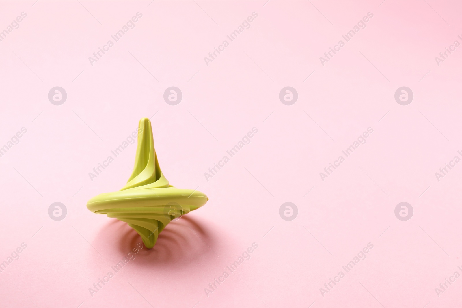 Photo of One green spinning top on pink background, space for text