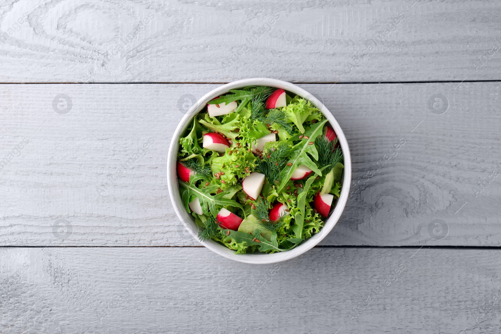 Photo of Delicious salad with radish, lettuce and arugula on light gray wooden table, top view