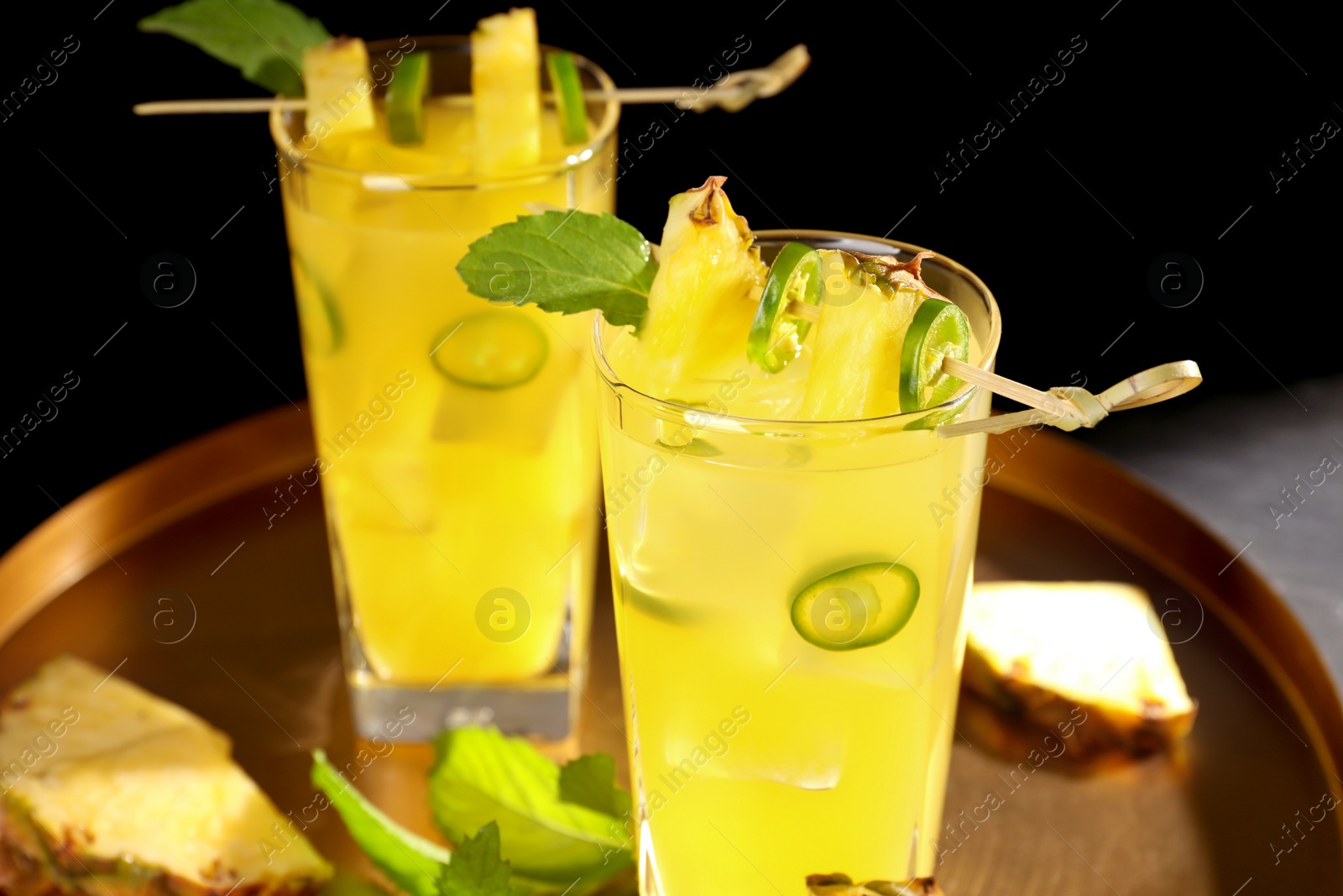 Photo of Glasses of tasty pineapple cocktail with sliced fruit, mint and chili pepper on tray, closeup