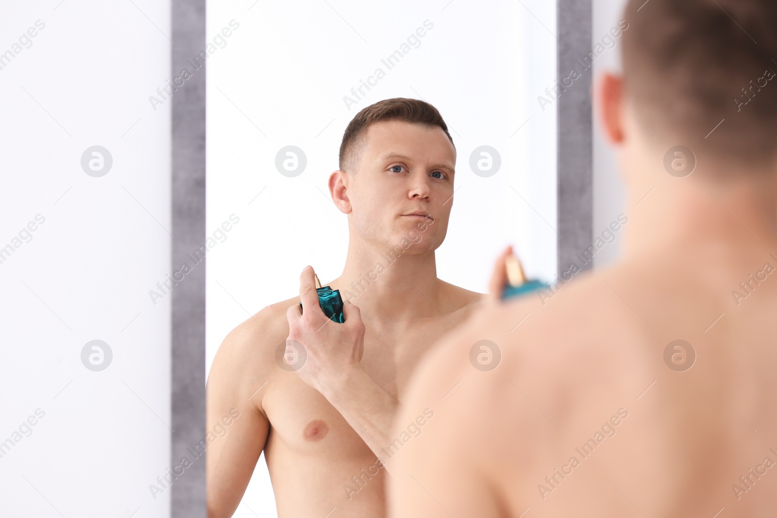 Photo of Handsome man using perfume in front of mirror