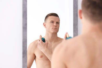 Photo of Handsome man using perfume in front of mirror