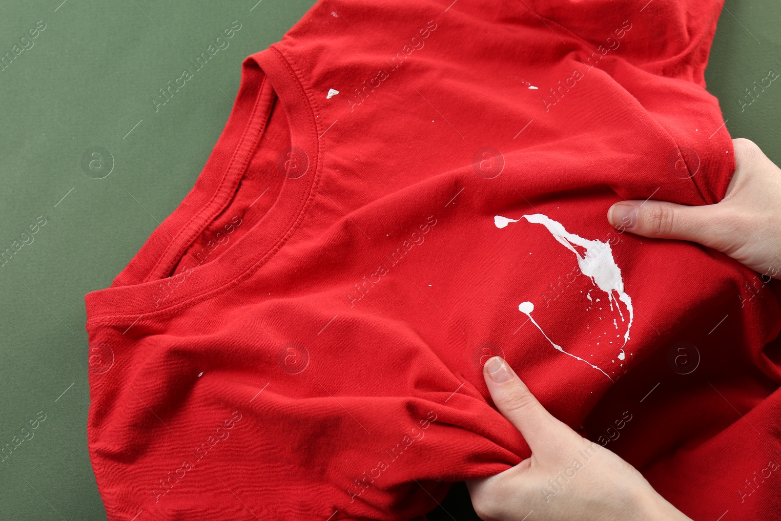 Photo of Woman holding red shirt with white paint stain on green background, top view