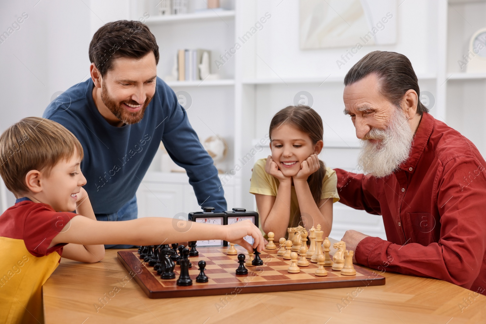 Photo of Family playing chess together at table in room