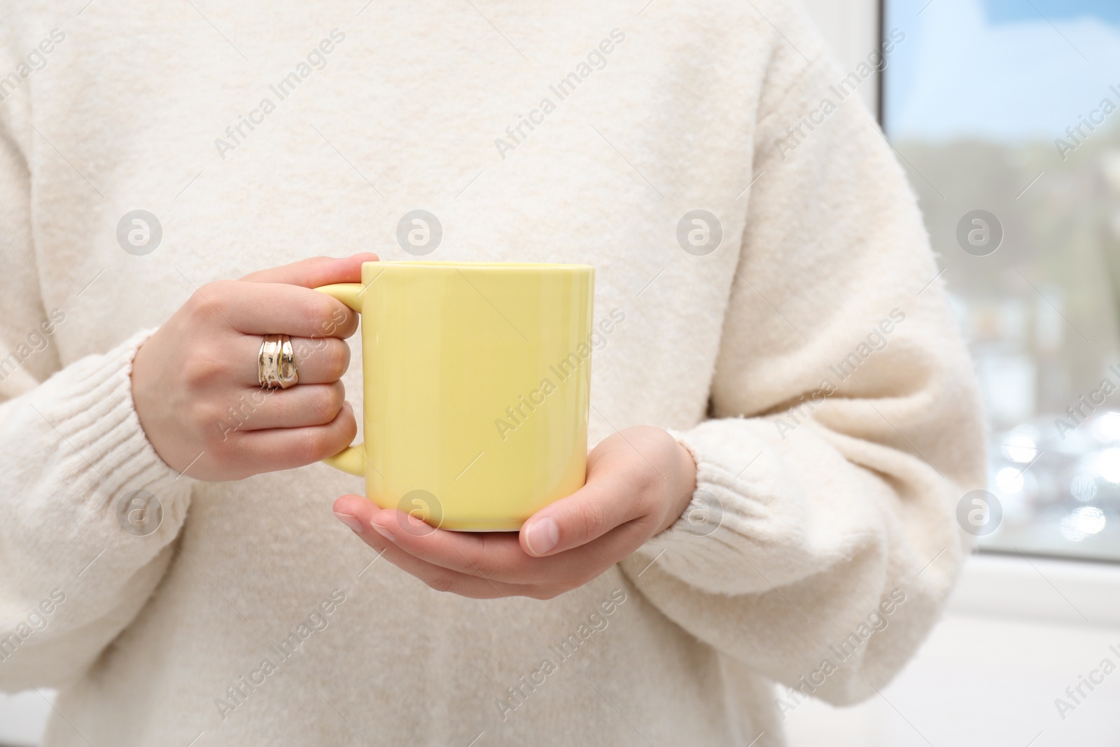 Photo of Woman holding yellow mug indoors, closeup. Mockup for design