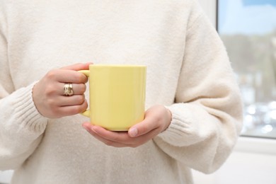 Photo of Woman holding yellow mug indoors, closeup. Mockup for design