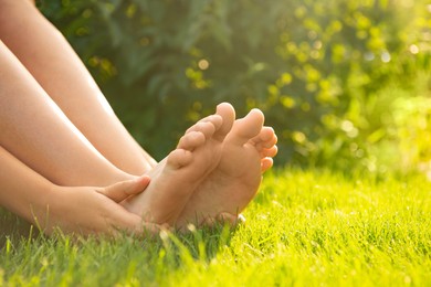Photo of Teenage girl sitting barefoot on green grass outdoors, closeup