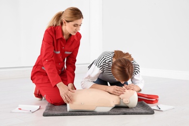 Photo of Instructor and woman practicing first aid on mannequin indoors