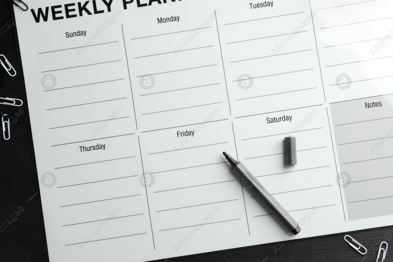 Photo of Timetable. Weekly planner, felt pen and paper clips on black wooden table, top view