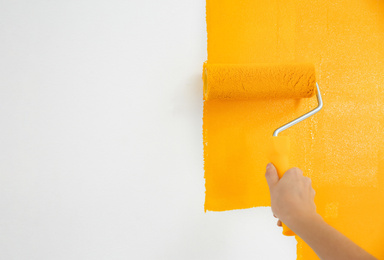 Photo of Woman painting white wall with yellow dye, closeup. Interior renovation