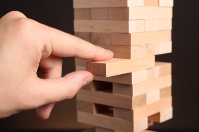Playing Jenga. Man removing wooden block from tower on dark background, closeup
