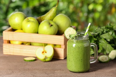 Mason jar of fresh green smoothie and ingredients on wooden table outdoors, space for text