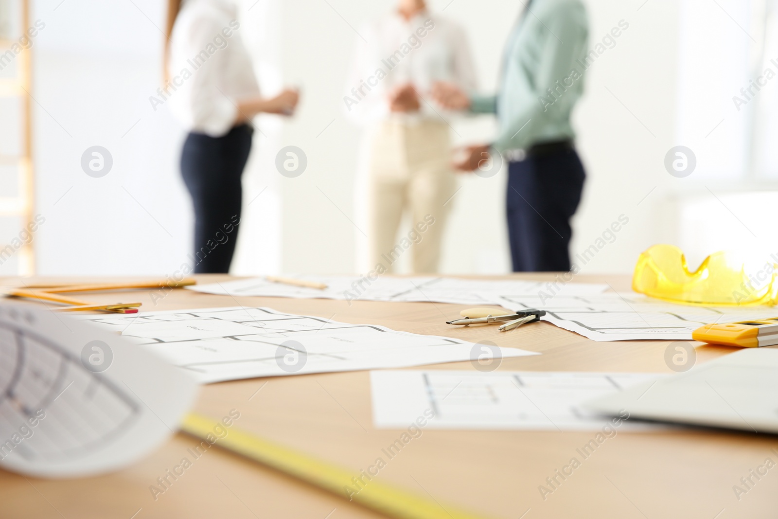 Photo of Colleagues in office, focus on table with construction drawings and tools