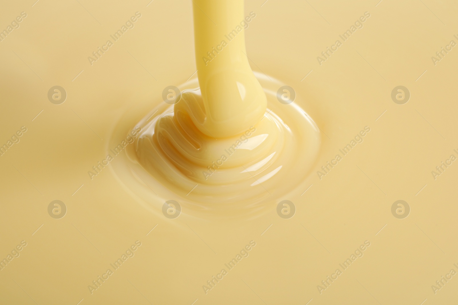 Photo of Tasty pouring condensed milk as background, closeup. Dairy product