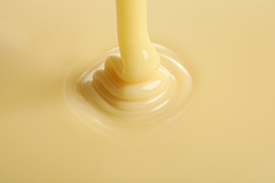 Photo of Tasty pouring condensed milk as background, closeup. Dairy product