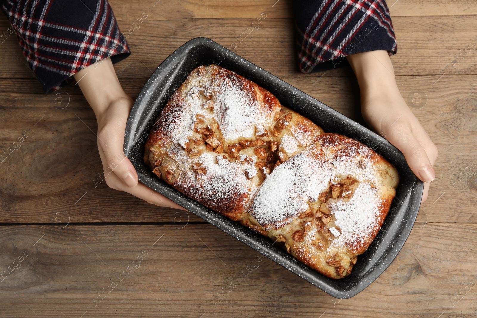 Photo of Woman holding baking pan with delicious yeast dough cake at wooden table, top view